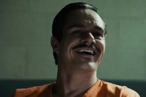 Lalo Salamanca ler skrattande i en orange fängelsedräkt, hans mustasch framträder tydligt.