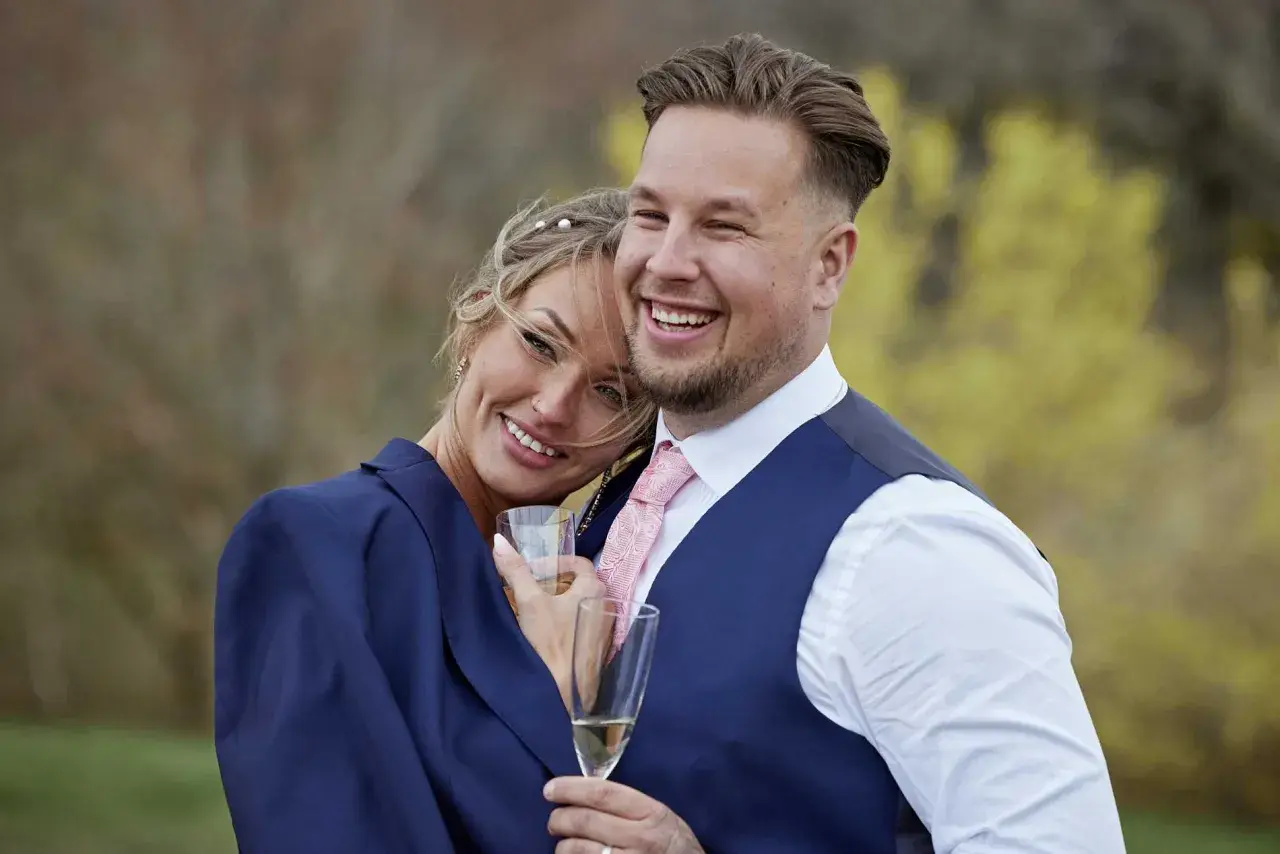 Ett lyckligt par, som från Love is Blind, firar med champagne. Rasmus ler stort, hans partner lutar sig mot honom.