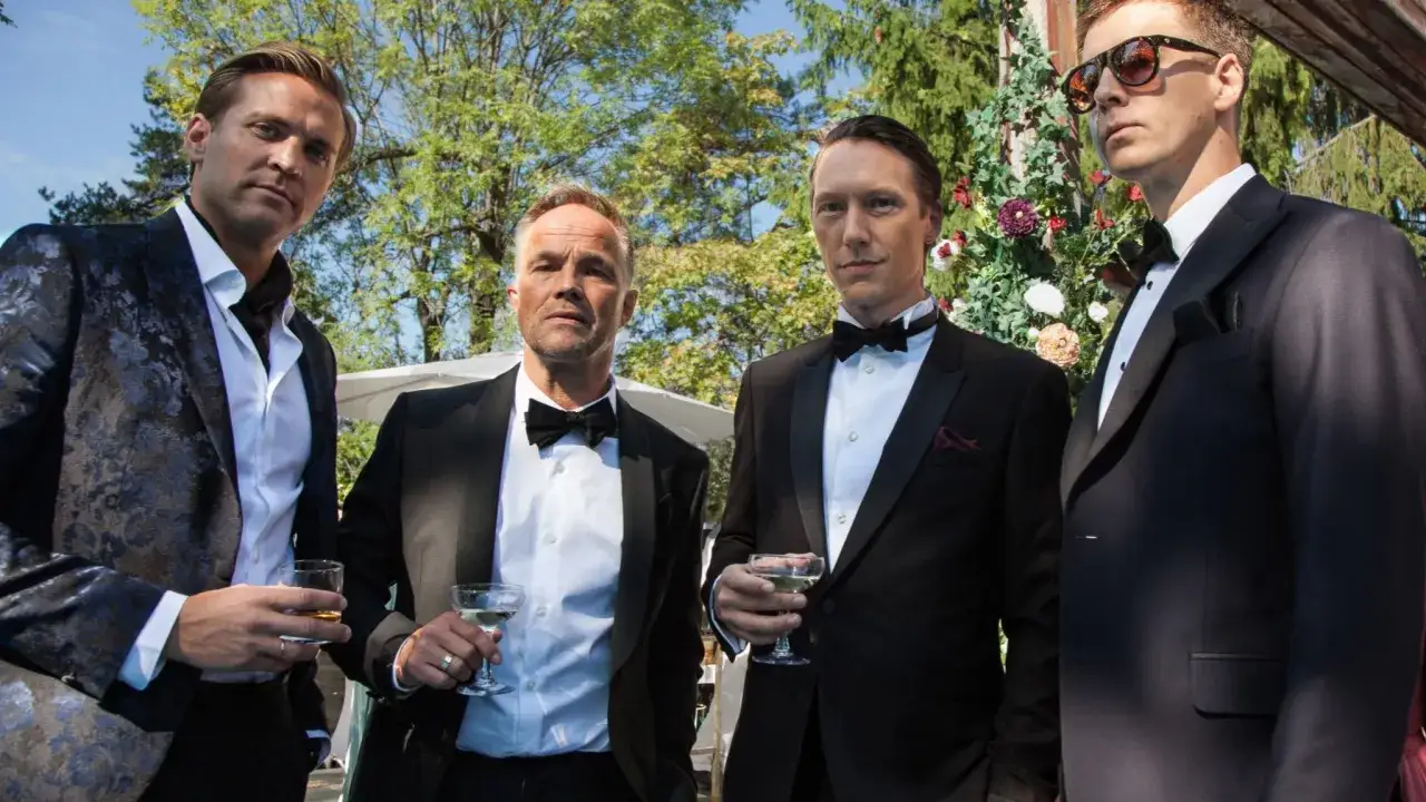 Fyra män i kostym, med drinkar i handen, ser ut som karaktärer från en norsk serie.