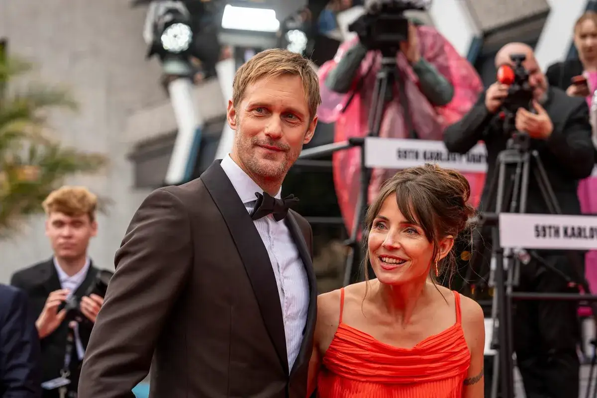 Alexander Skarsg&aring;rd och Tuva Novotny p&aring; r&ouml;da mattan, omgivna av fotografer.