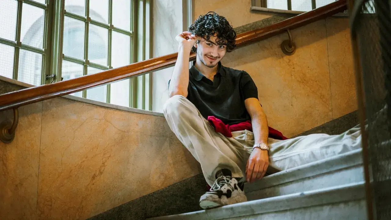 Malte Gårdinger sitter på en trappa med lockigt hår och ett leende.