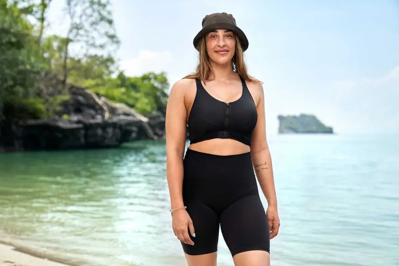 Sandra Cucarano p&aring; en strand med gr&ouml;na &ouml;ar i bakgrunden. Hon b&auml;r en svart bikini och en hatt.