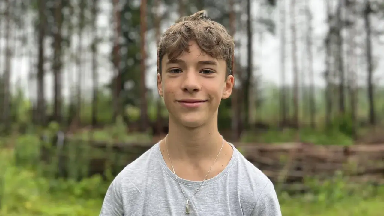 En leende Jack Bergnorth Henriksson står framför en skog med träd och grönskande buskar.