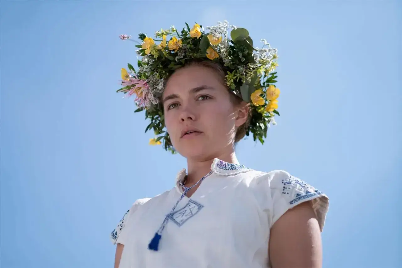 En kvinna med blomsterkrans b&auml;r en broderad kl&auml;nning. Hon &auml;r en del av rollistan i midsommarfilmen.