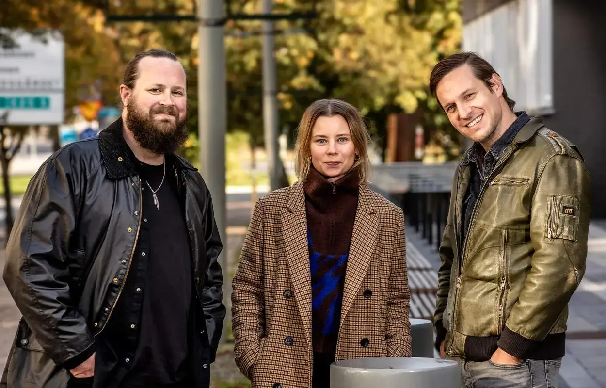 Tre personer, tv&aring; m&auml;n och en kvinna, ler mot kameran. De ser ut att vara sk&aring;despelare fr&aring;n en ny svensk serie.
