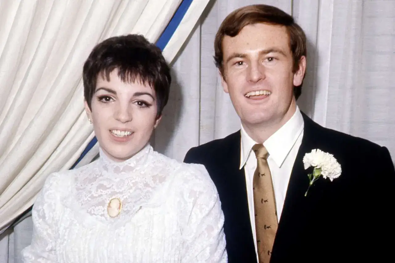 Liza Minnelli i hennes make, Peter Allen, ler mot kameran. Liza bär en vit spetsklänning med en brosch.