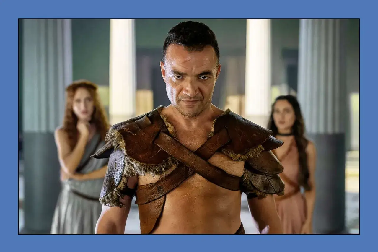 En man i l&auml;derrustning, med tv&aring; kvinnor i bakgrunden, fr&aring;n Spartacus: House of Ashur.